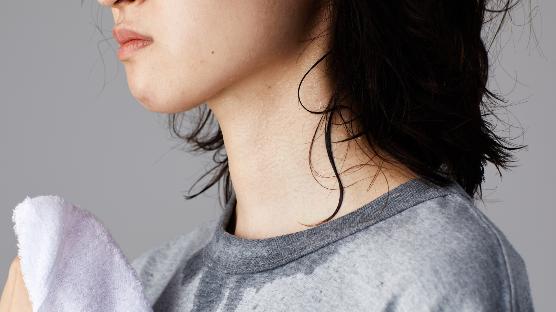 Close-up of a woman with visible neck sweating and damp clothing, illustrating menopause night sweats and hot flash symptoms during perimenopause.