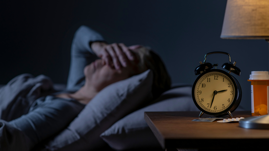 Woman over 40 lying awake at 2 a.m. with alarm clock and sleep medication, experiencing perimenopause insomnia and nighttime awakenings