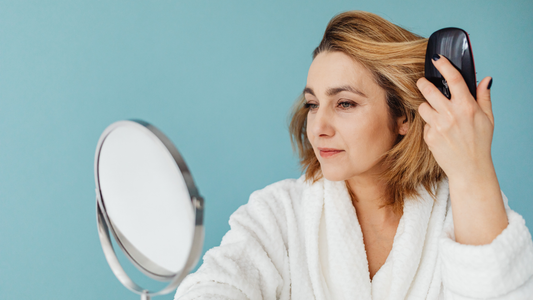 Woman over 40 brushing her hair and looking in a mirror while noticing possible hair thinning during perimenopause or menopause.